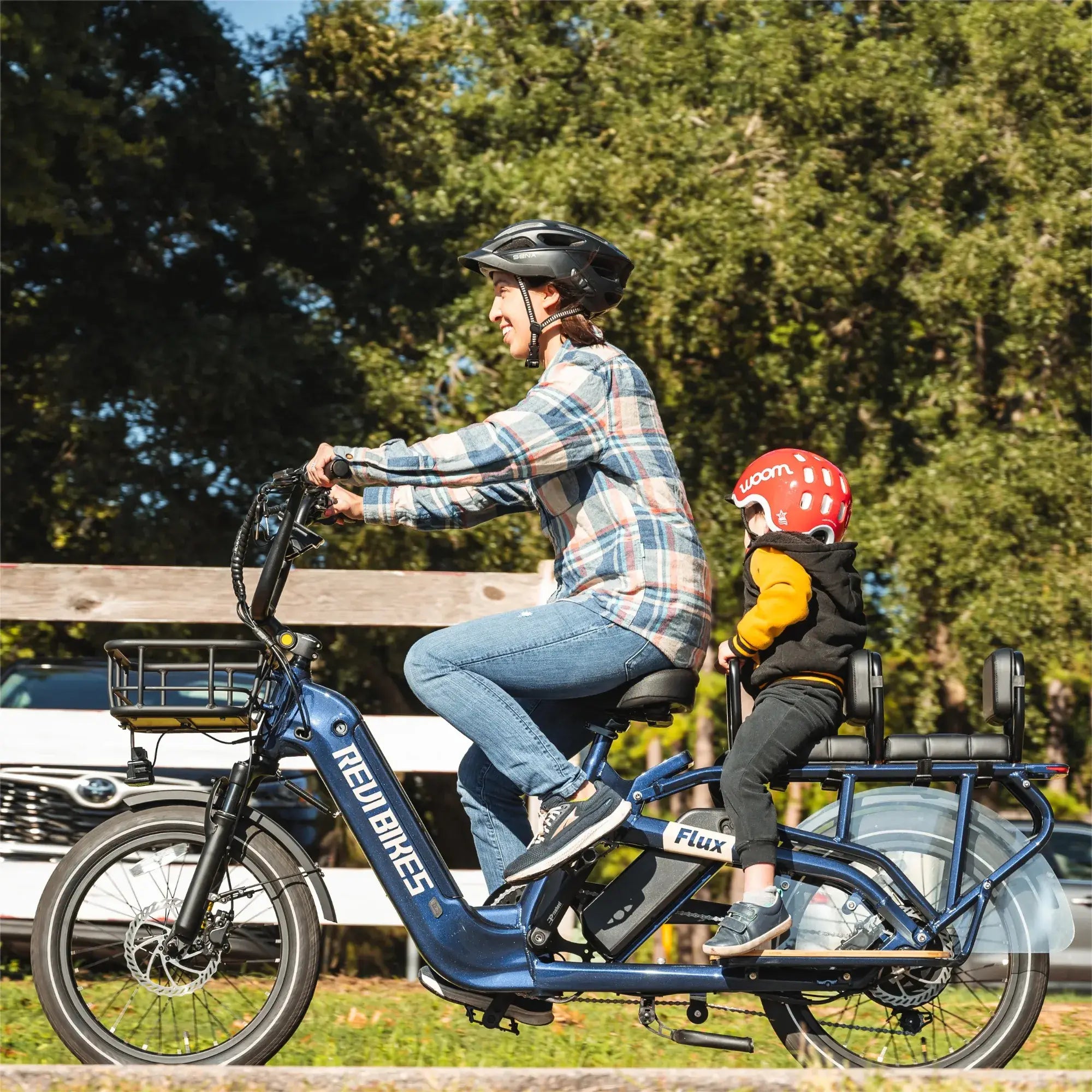 Man and child riding a blue cargo bike in a park