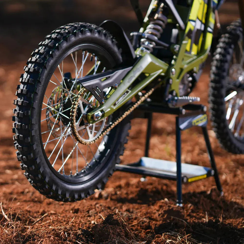 Close-up of a surron 2025 lightbee x  dirt bike tire and suspension on a stand with a dirt background