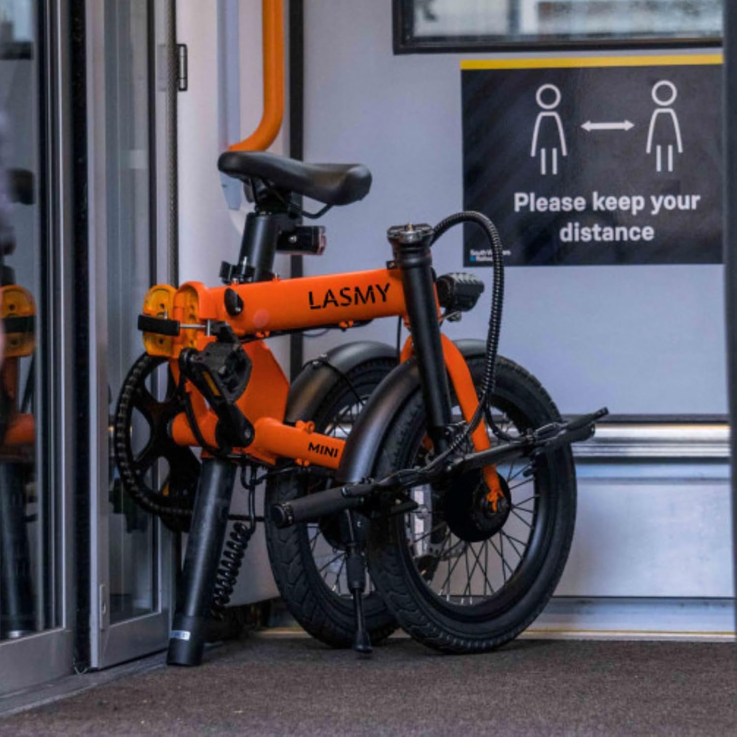 orange lasmy mini folding ebike in the subway corner