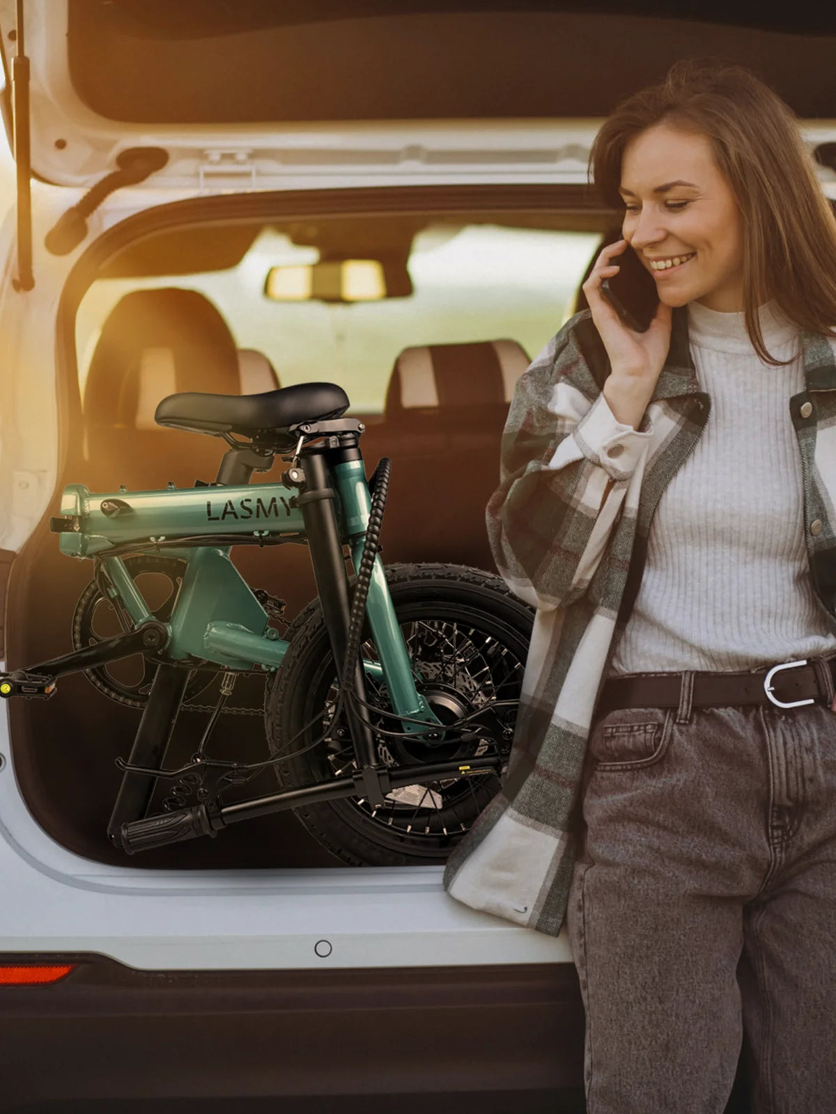 Woman talking on a phone next to lasmy folding electric bike in the back of a car