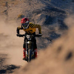 Person riding a ultrabee dirt bike on a dusty track with mountains in the background