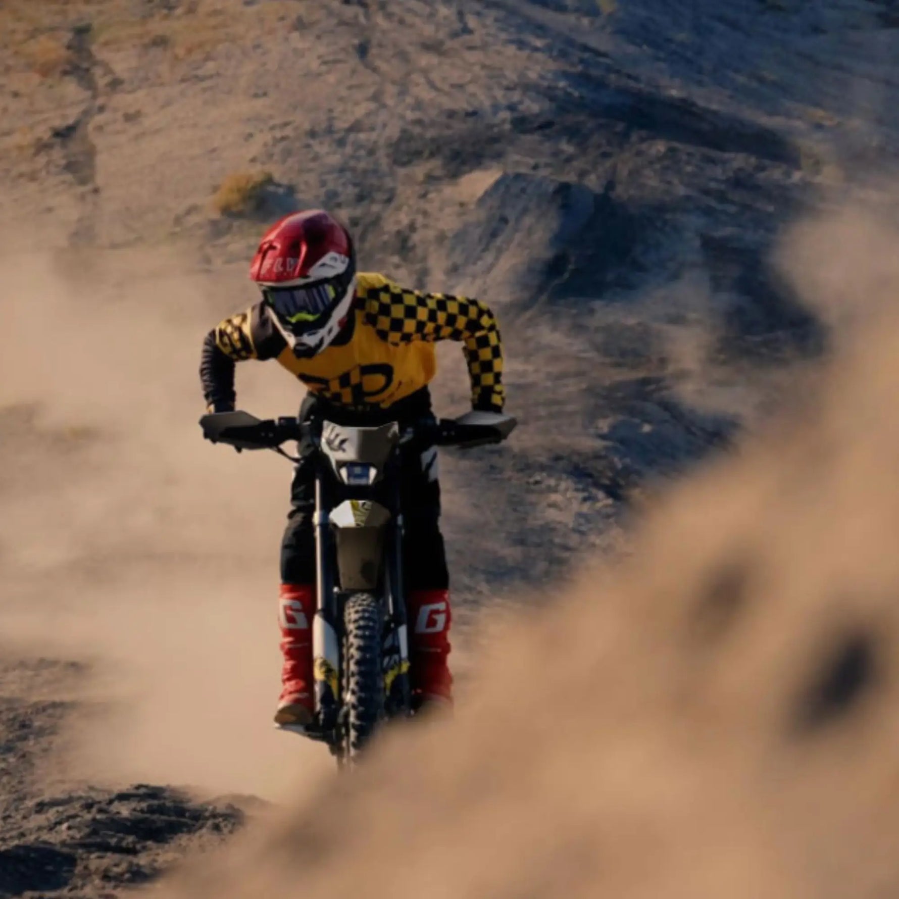 Person riding a ultrabee dirt bike on a dusty track with mountains in the background